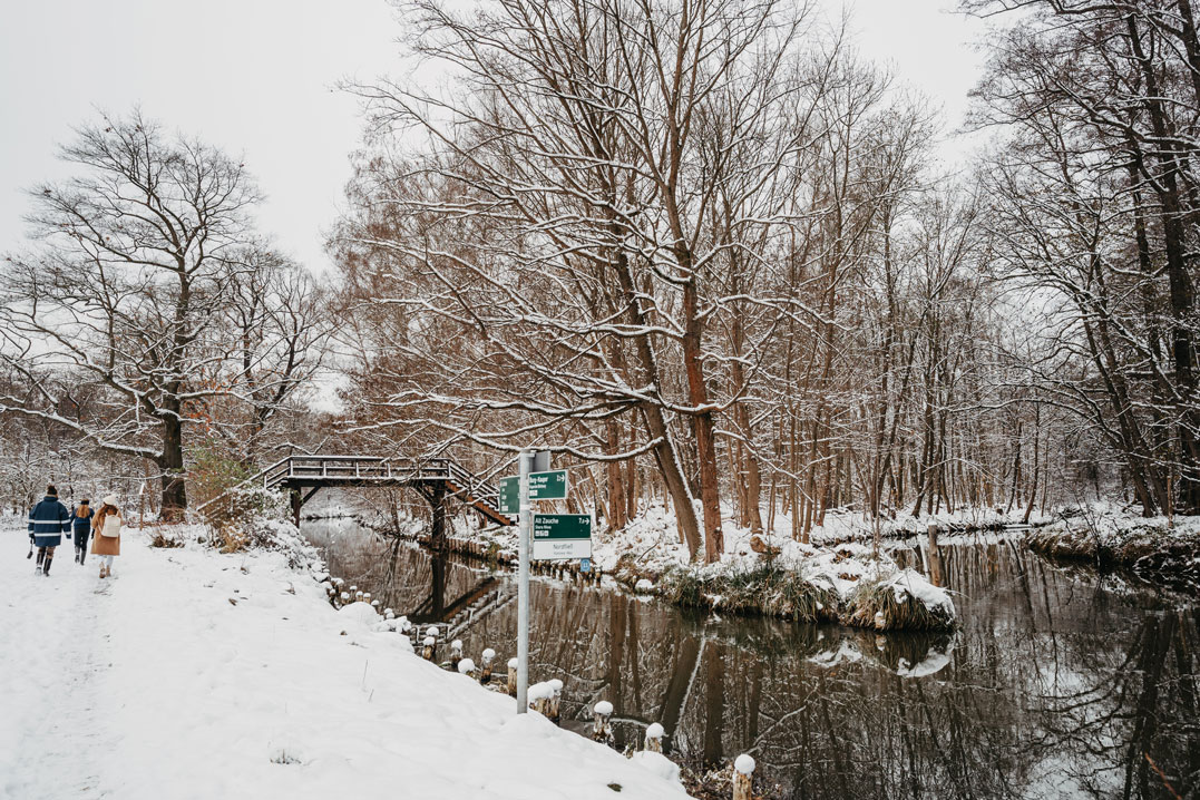 Kanal mit Holzbrücke in verschneitem Wald